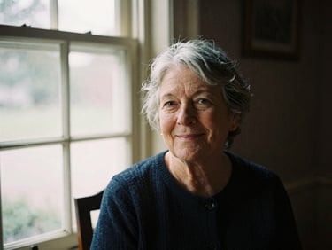 A warm 35mm film portrait of an older New England woman with gray hair smiling gently, soft natural window light, historic indoor setting.