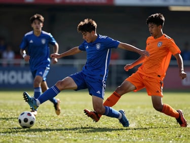 Dynamic shot of youth soccer players mid-action, diving for a ball, dramatic natural sunlight, low angle, vibrant cobalt and orange tones, sharp focus, 35mm