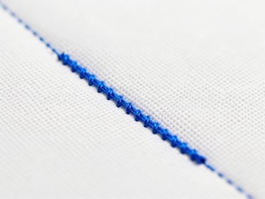 Macro shot of electric blue thread being embroidered onto structured white canvas, clean stitches, high-key studio lighting, 35mm
