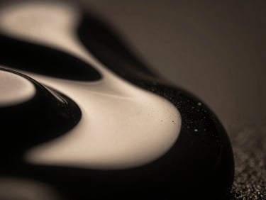 Extreme close-up macro texture of liquid obsidian reflecting warm cream studio light, dramatic chiaroscuro