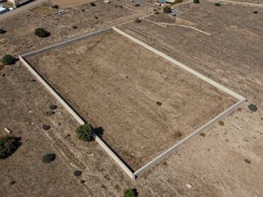 Close aerial framing of a rectangular land parcel in Turkey, boundary markers visible at corners, surrounding dry earth and sparse vegetation, architectural survey perspective, natural daylight, no people