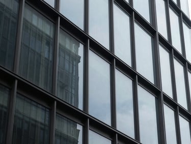 A tight, abstract architectural crop of high-contrast steel and tinted glass facade reflecting cool, diffused daylight, 35mm editorial photography.