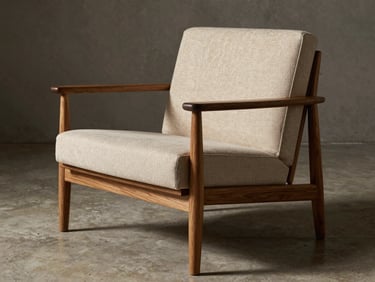 Warm editorial photography of a minimalist lounge chair with solid wood frame and premium textured upholstery, concrete studio setting, dramatic side-light, 35mm