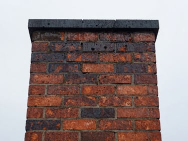 Water beading on a waterproofed brick chimney surface after rain, overcast sky.