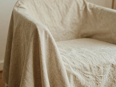 Detail of textured beige linen fabric draped over a minimalist chair, soft shadows, warm editorial feel.