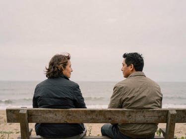 A quiet environmental portrait of two neighbors talking on a wooden bench, soft overcast coastal daylight, muted earth tones, natural 35mm film grain.