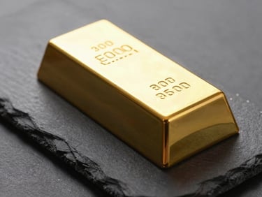 A close-up of a pure gold bar resting on a dark slate surface, dramatic side lighting highlighting the stamped purity markings.