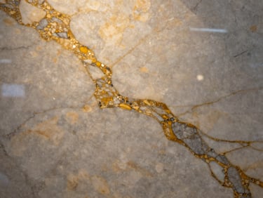 Macro shot of premium Italian Calacatta marble slab, rich golden and grey veins, polished texture, dramatic side lighting highlighting the stone details.