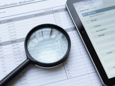 Close-up, crisp corporate photography, cool overcast daylight, desaturated blue and slate tones, sharp focus, 35mm, a magnifying glass over a printed audit log, next to a tablet displaying a digital audit trail, highlighting specific entries.