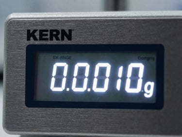 Extreme macro close-up of a KERN scale digital display, sharp glowing white numbers showing 0.0000g, dark brushed aluminum housing, clinical laboratory setting.