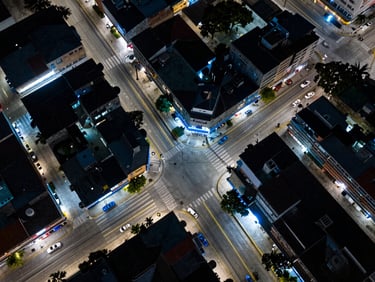 Overhead drone shot of Puerto Boyacá urban grid with visible network cable infrastructure running along streets, sharp blue ambient light, technical overhead framing