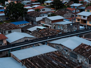 Overhead view of a mid-sized Colombian town neighborhood with fiber-optic cable conduits visible along rooftops, cool studio lighting, crisp technical framing