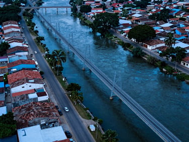 Overhead shot of Puerto Berrío riverfront town with fiber network infrastructure visible along streets, sharp cool blue lighting, technical precision framing