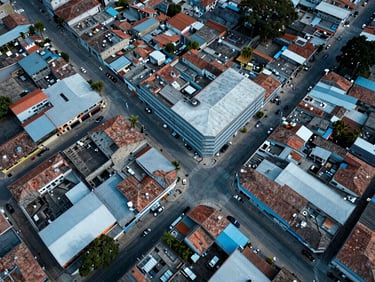 Overhead drone view of Colombian mid-size municipality rooftops and street grid with network cable infrastructure visible, sharp studio lighting, crisp blue tones