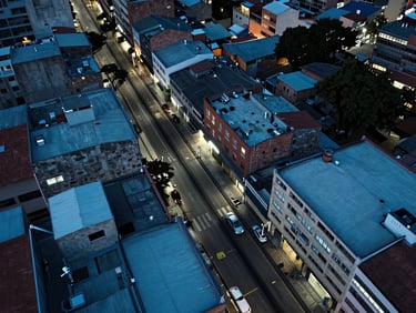 Overhead drone view of Medellín urban rooftops and fiber cable infrastructure running along streets, sharp edges, cool blue ambient light, technical and precise