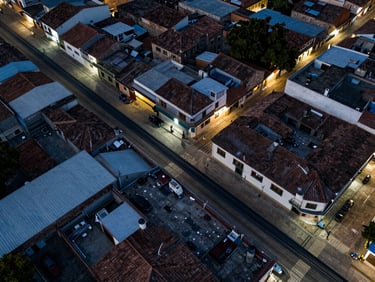 Aerial view of Cáceres Colombia town layout with fiber optic cable conduits along rooftops, cool ambient technical light, precise overhead framing