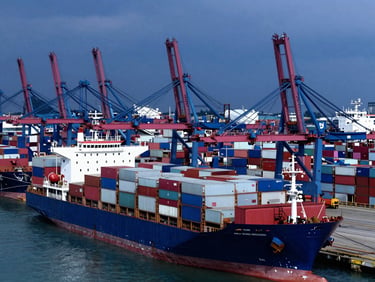 High-contrast overhead shot of cargo ships docked at a busy Jakarta port terminal under dramatic overcast daylight, sharp focus, industrial blue tones, 35mm