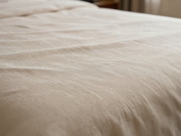 Extreme close-up of hotel bed sheet weave structure on an inspection table, threads clearly visible under diffused strobe light. Warm ivory fabric, crisp thread-level detail. No people, no text.