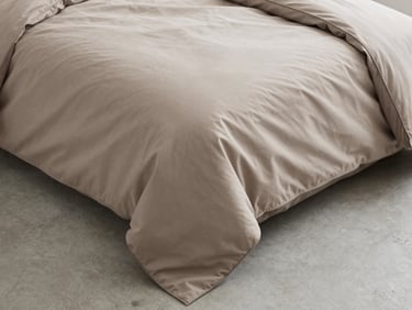 Wide overhead flat-lay of a neatly folded duvet cover on a clean concrete surface, corner seam detail visible under diffused window light. Pale taupe tones, precise fold lines. No people.