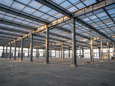 Wide-angle interior view of a massive completed steel frame warehouse, clean concrete floor, natural light filtering through translucent panels