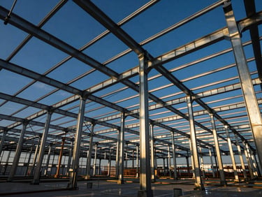 Wide-angle interior shot of a massive steel frame warehouse under construction, blue sky visible through beams, sharp architectural lines, dramatic sunlight