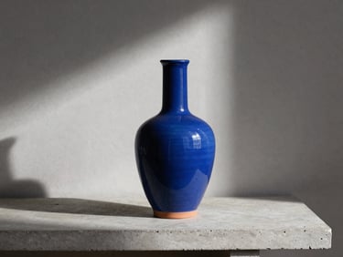 Artisanal Jaipur Blue Pottery styled in a contemporary American living room, minimalist ceramic vase on a concrete console, soft directional side light.