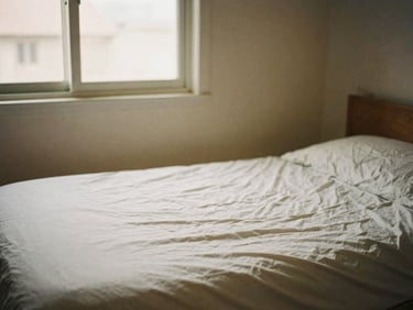 Neatly made bed in a clean, simple bedroom, warm natural light from a window, no personal belongings visible, no faces, 35mm film style.
