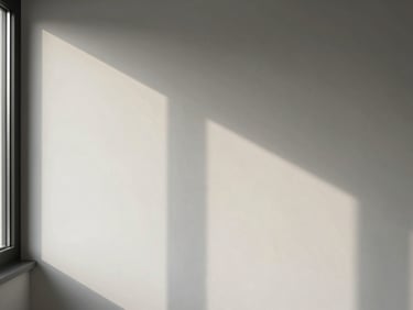 Corner of a room where a window casts a long, soft shadow across a white wall, showing the subtle transition of daylight. Editorial architectural photography, sharp details.