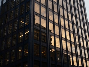 Wide architectural shot of a modern financial district building facade reflecting abstract geometric light patterns, overcast exterior light, editorial corporate photography, deep navy and warm gold tones, high contrast.