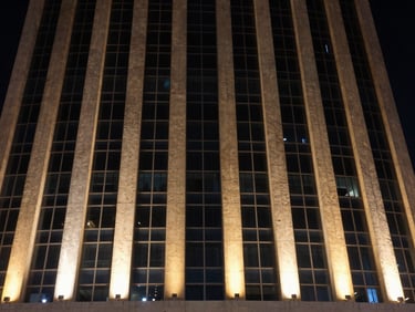 Dramatic night view of a modern skyscraper facade in Al Khobar, sharp amber LED grazing lights illuminating the textured concrete and glass exterior, medium format.
