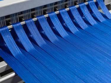 Macro close-up of high-speed needle looms weaving electric blue technical elastic bands, industrial factory environment, sharp focus on fiber texture