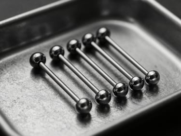 Studio shot of multiple sterile titanium piercing bars grouped on a dark metallic tray, high-contrast black and white, sharp reflections