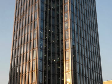Symmetric architectural shot of a modern glass and steel office tower, golden hour light reflecting off the facade.