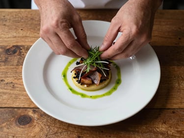 Extreme close-up overhead flat-lay of a plated dish mid-service on a worn wooden table, hands of a cook visible at the top edge adjusting a garnish, tungsten kitchen light warming the scene, natural shadows, no styling