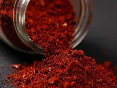 Macro shot of fine red chili powder cascading into a pristine glass jar, deep crimson tones, moody side-lighting
