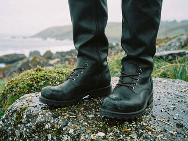 Close up of leather walking boots on wet granite stone covered in green moss, soft overcast daylight, 35mm film