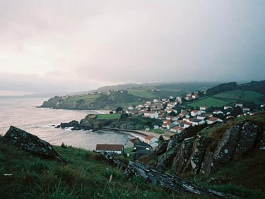 View from Mirador de Chao de Monte overlooking the misty Galician coastline and the village of San Andrés de Teixido, soft light of coastal sunset, 35mm film
