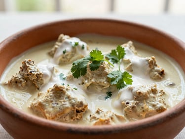 Close-up of creamy Butter Chicken in a rustic ceramic bowl, garnished with fresh cream and cilantro, soft natural light.