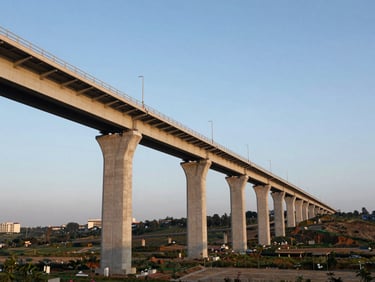 Wide environmental photograph of a completed light rail transit viaduct stretching across an urban valley, photographed from the end of the alignment, golden-hour light, steel deck and concrete piers sharp against clear sky