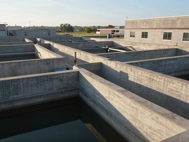 Ground-level wide angle of a municipal water treatment facility, large concrete basin structures visible, crisp morning light, no people, geometric forms and precise construction joints emphasized