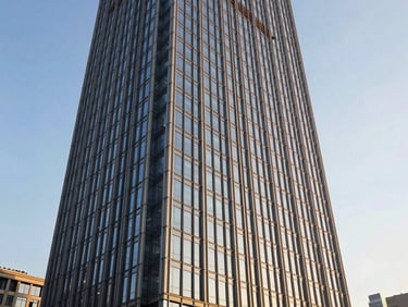 Wide environmental shot of a completed 52-story glass-and-steel commercial tower photographed from street level, sharp golden-hour side light emphasizing curtain wall geometry and structural grid, clear sky
