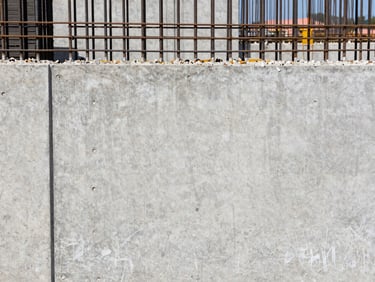 Straight-on architectural shot of a newly cast concrete wall and steel reinforcement bars, bright natural daylight, high-contrast industrial tones, sharp focus, 35mm lens