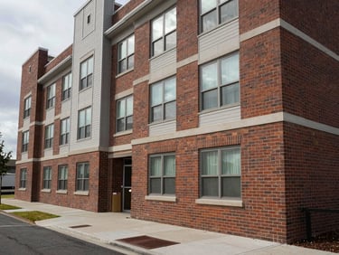 Wide environmental shot of a completed mid-rise apartment building exterior, soft overcast light, brick and panel facade in sharp detail, empty sidewalk foreground establishing scale