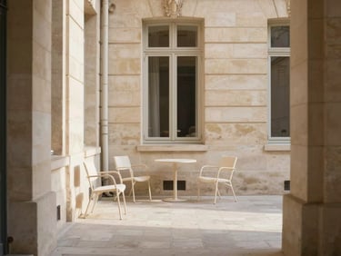 A quiet paved Parisian courtyard surrounded by stone walls, elegant minimalist outdoor chairs, soft warm sunlight, editorial architectural shot