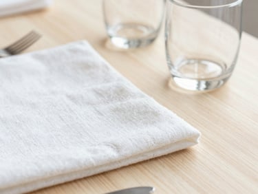 Bright editorial photography, soft natural daylight, close-up of crisp linen textures and polished glassware on a clean wooden table, 35mm lens