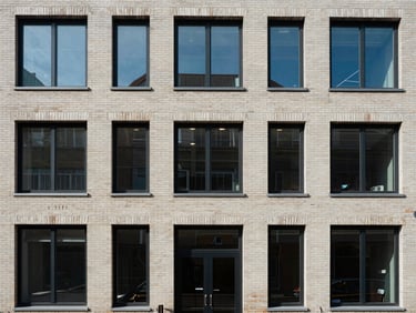 Close-up of a residential building facade straight-on, clean brick and glass exterior, north-facing flat light, no people, architectural detail of windows and entry door visible, urban street edge at bottom of frame