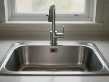 Close-up of a kitchen countertop with stainless steel sink and stone surface under diffuse window light, no people, clean and empty, straight-on framing