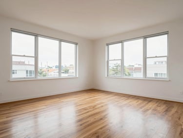 Wide interior shot of a clean two-bedroom apartment, north-facing daylight through large windows, hardwood floors visible, empty living room with white walls