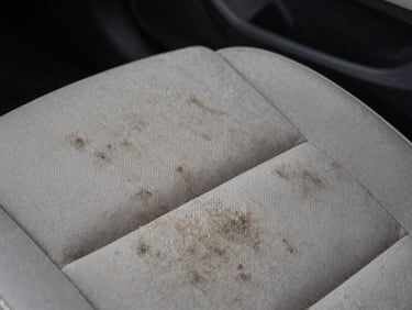 Close-up of automotive interior upholstery fabric showing embedded dirt and staining before chemical cleaning, controlled studio lighting from above revealing fiber texture and contamination depth