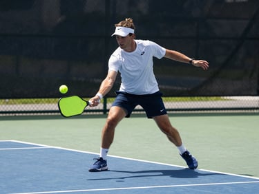 Action shot of an active player mid-rally hitting a neon pickleball, bright outdoor court daylight, dynamic court-level composition